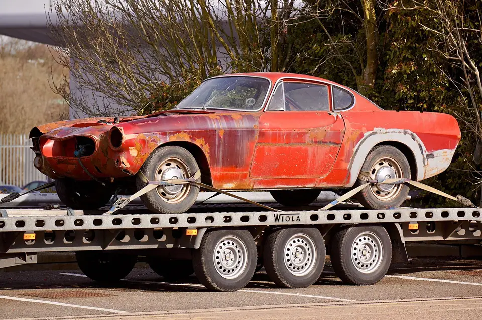 A rusted old coupe strapped down on a flatbed trailer